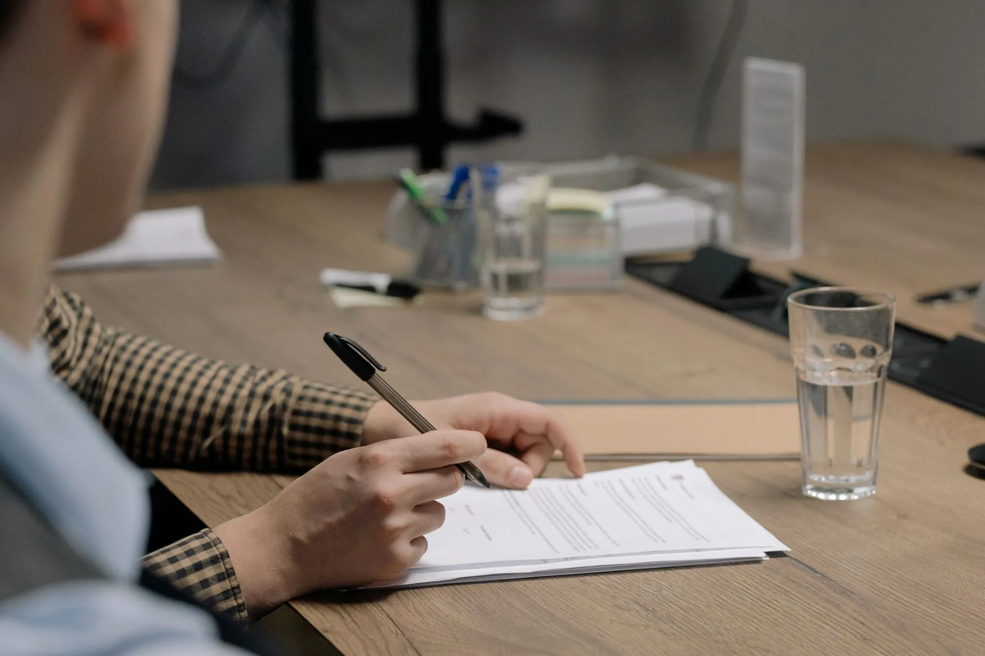 Persoon in kantoorkledij die aan een houten tafel een document ondertekent